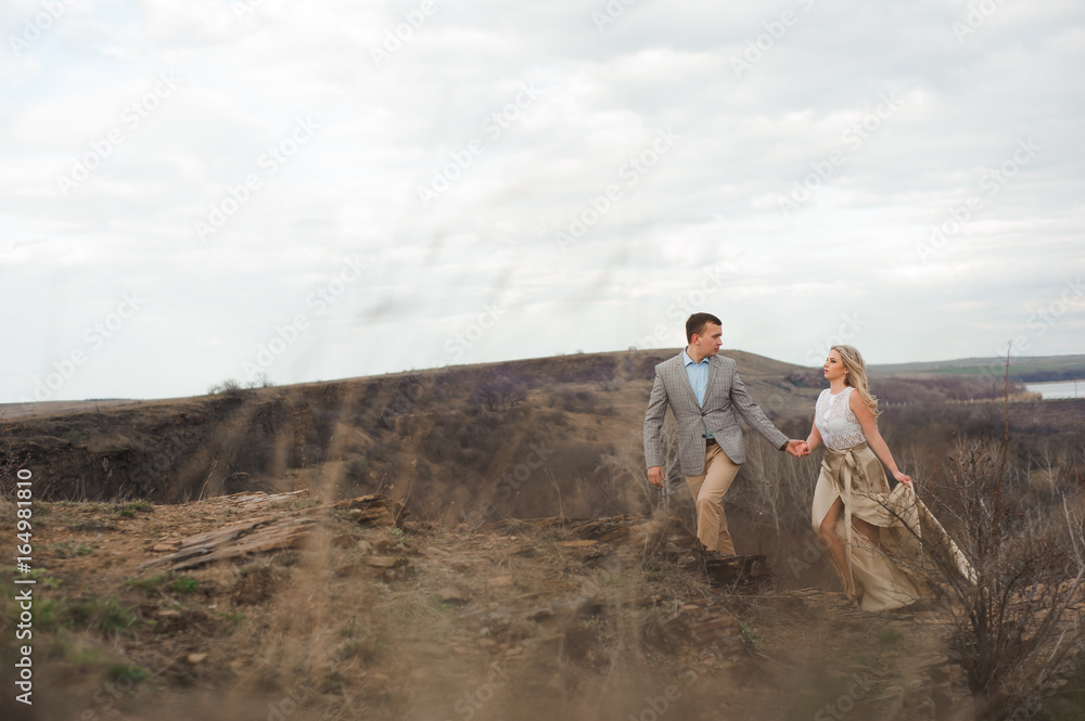 Handsome guy and blonde girl walking on the field, a man leads a woman holding the hand Handsome guy and blonde girl walking on the field, a man leads a woman holding the hand