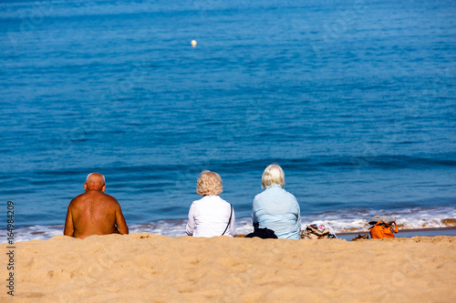 family sitting on beach towels in the sand. Three persons, one man and two women. 