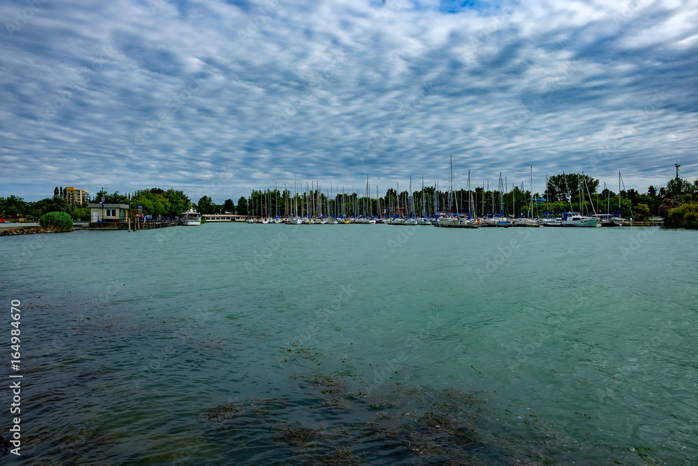 sailing harbor at Balaton lake summer holiday starts - cloudy sky, green water, sailing boats in background