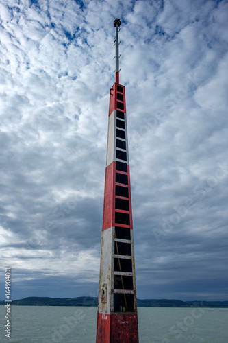 harbor light tower shows the way for sailboats - white, red colored metal tower with cloudy stormy sky and Balaton lake in background