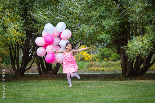 Charming little girl in a smart pink dress runs to meet with a big bunch of pink balloons.