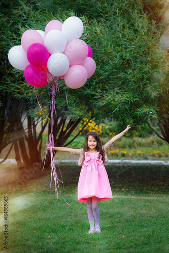 Charming little girl in a smart pink dress stand with a big bunch of pink balloons.