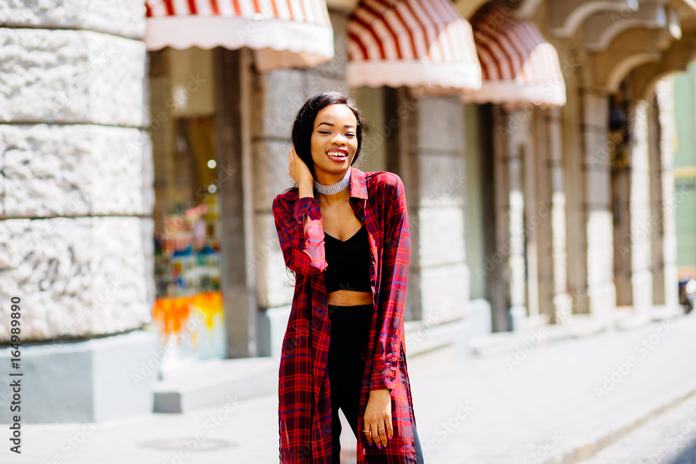 Fototapeta premium Young gorgeous African American woman in trendy summer outfit posing confidently on the sity street, outdoors.