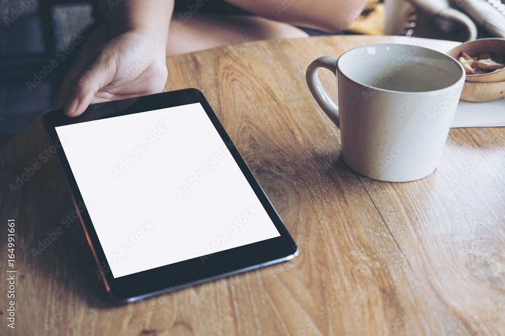 Mockup image of hands holding , showing and giving black tablet pc with blank white screen to somwone on vintage wooden table with coffee cup