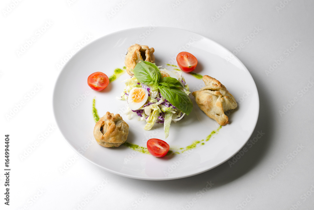 Salad with pies and lettuce leaves on a white plate