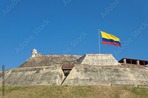Colombian flag is streaming in the wind over the weathered walls of the fortress of Castillo San Felipe de Barajas in Cartagena de Indias, Colombia.