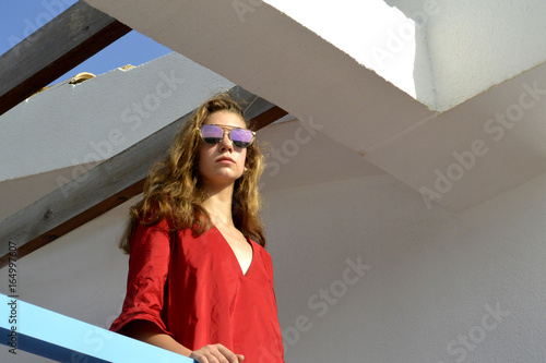 La chica rubia con pelo largo con gafas del sol en vestido rojo esta en la terraza abierta   photo