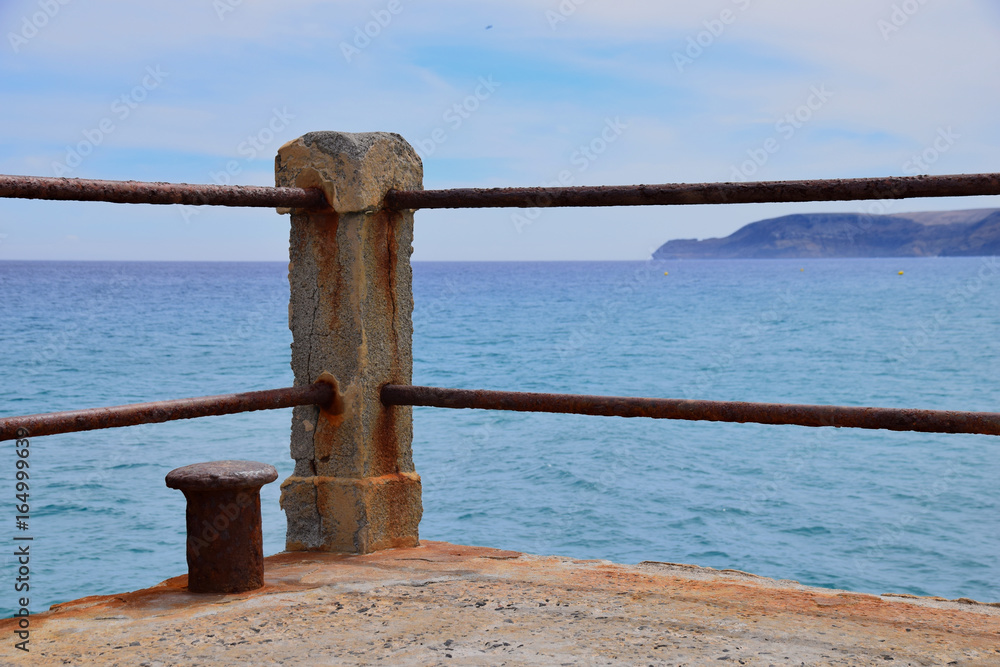Fototapeta premium Concrete post of rusty ship bollard at the end of a concrete pier overlooking the Atlantic Ocean