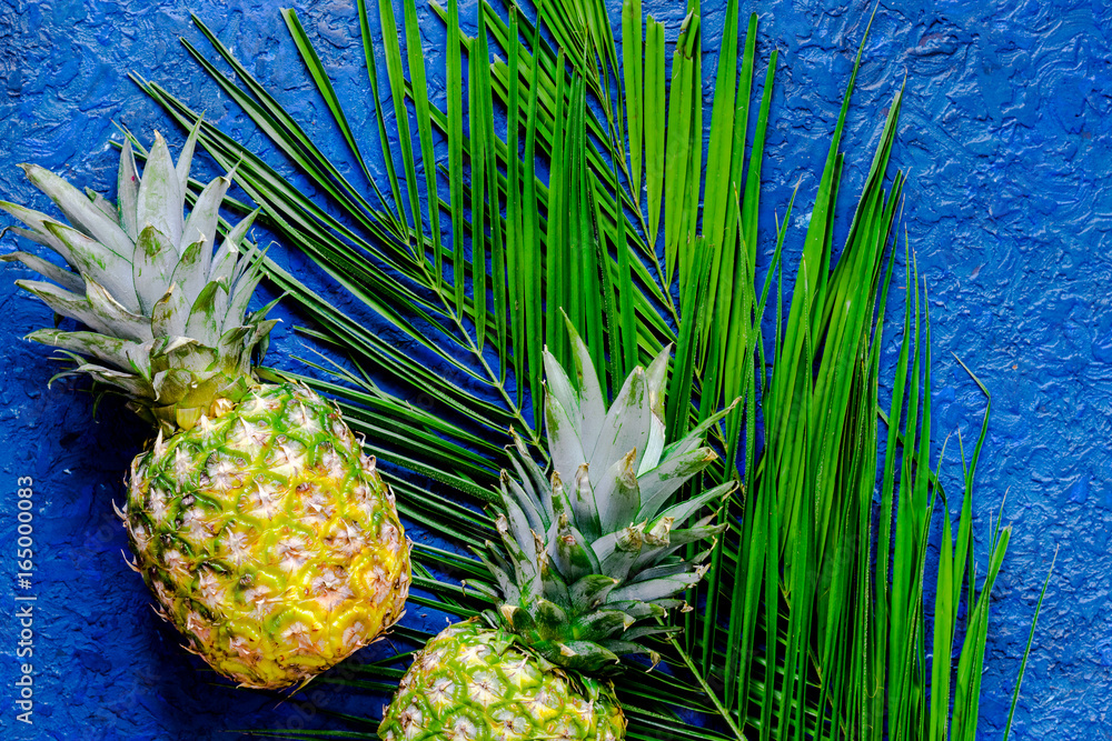 Fototapeta Pineapple and palm branch on blue table background top view