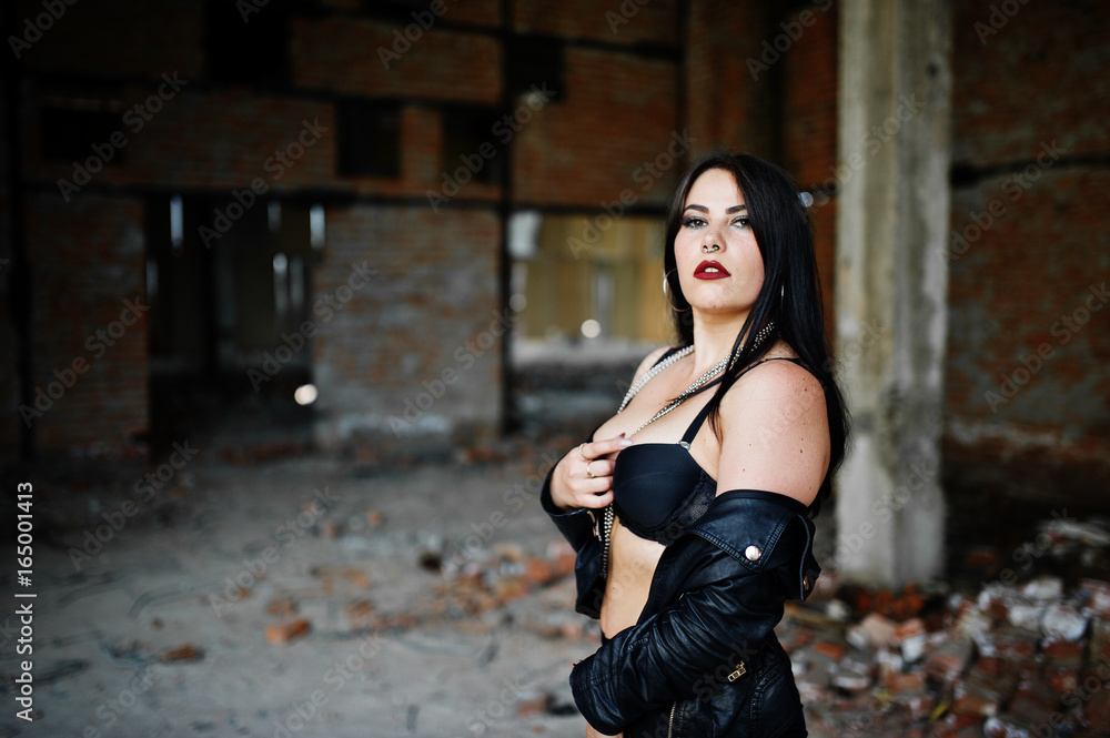 Fototapeta premium Brunette plus size sexy woman with earring in the nose, wear at black leather jacket, lace bra at abadoned place.