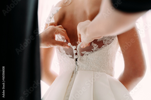 Bridesmaid helps fasten a wedding dress the bride before the ceremony. Wedding concept photo