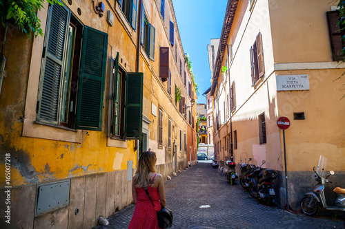 Girl in red dress walking on Rome street. Trastevere, Rome, Italy. Young girl. Old street in Rome. Pretty girl around the corner. Rome architecture. Blonde hair girl © Epic Vision