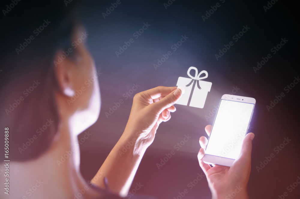 Image of a woman with a smartphone in her  hand. She gets a gift. Concept of gift in the age of digital technology. - obrazy, fototapety, plakaty 