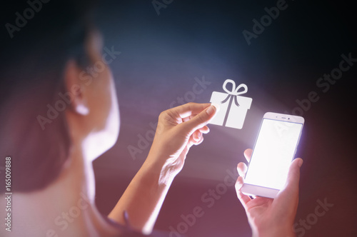 Image of a woman with a smartphone in her  hand. She gets a gift. Concept of gift in the age of digital technology.