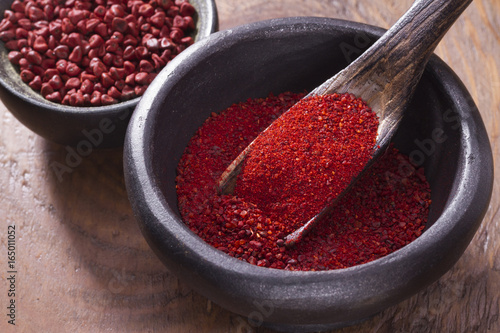 Achiote grains and powder in wooden bowl photo