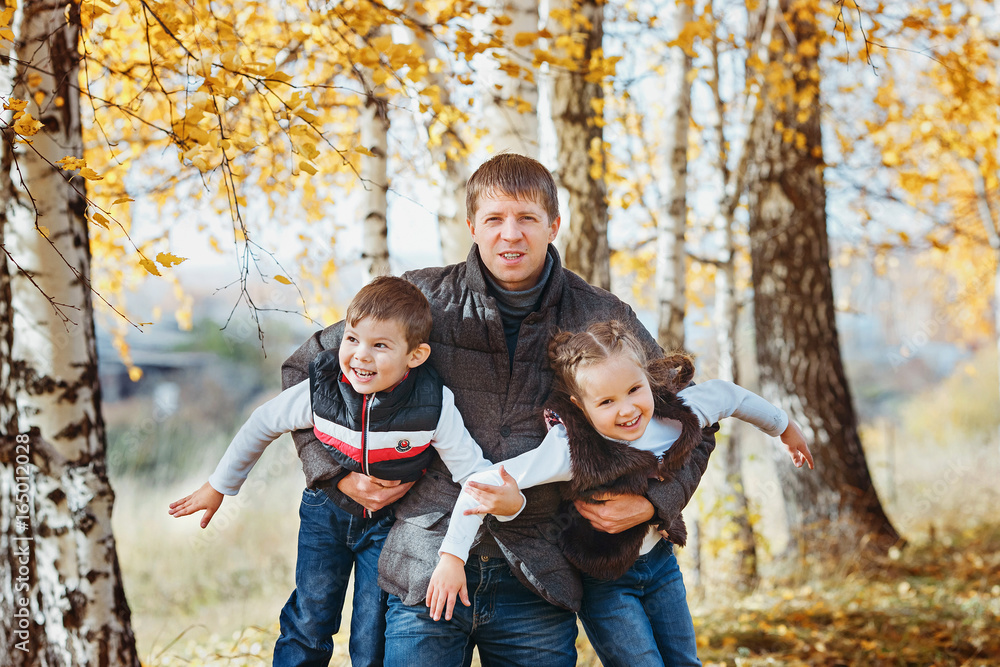 Father holds on hands and circling two laughing children in the autumn birch forest. Close-up Father holds on hands and circling two laughing children in the autumn birch forest. Close-up