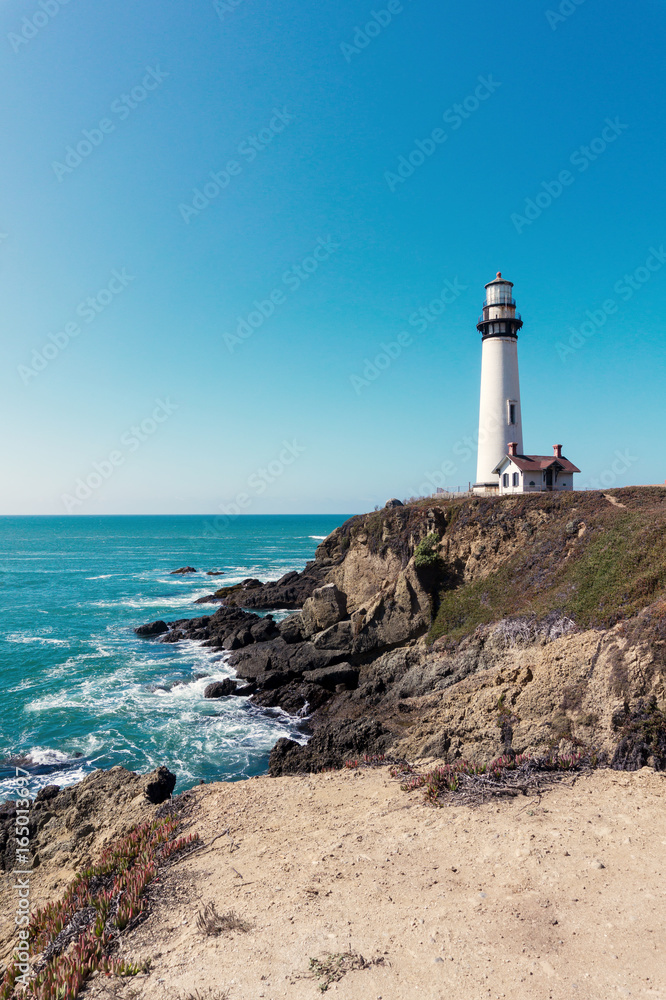 Lighthouse near the caost highway in California USA with a blue sky and rocky shore.