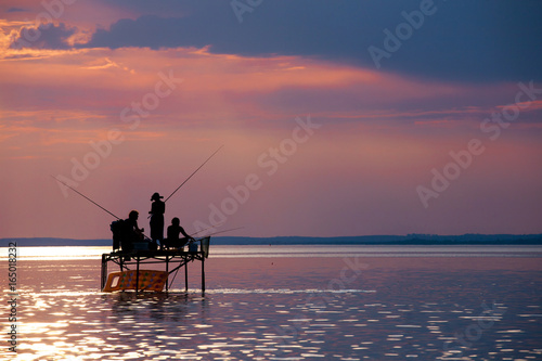 Anglers' silhouettes on a fishing stand at sunset at Lake Balaton, Hungary