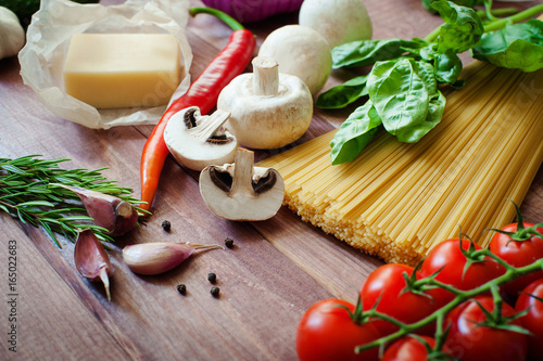 Italian food background, with vine tomatoes, basil, spaghetti, mushrooms, parmesan, garlic, peppercorns, rosemary, parsley and thyme. Wooden background.