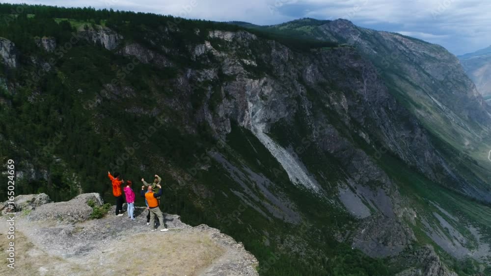 Climbers on summit. Happy people embracing raising hands up on pointed rocky cliff blue sky background aerial slow motion 4k Climbers on summit. Happy people embracing raising hands up on pointed rocky cliff blue sky background aerial slow motion 4k