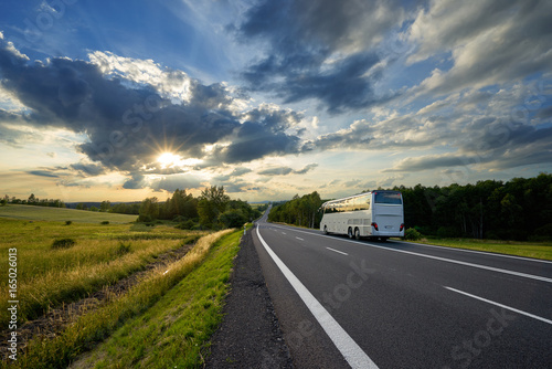Obraz na płótnie Bus traveling on the asphalt road in a rural landscape at sunset with dramatic clouds w salonie