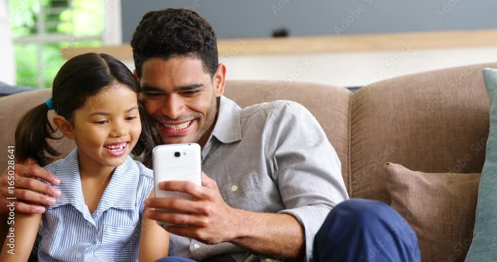 Father and daughter using mobile phone in living room Father and daughter using mobile phone in living room