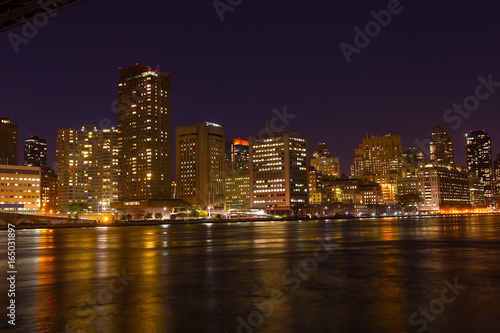 Manhattan skyscrapers with colorful reflections in East River at night. A view on Manhattan from Roosevelt Island at night in New York, USA.