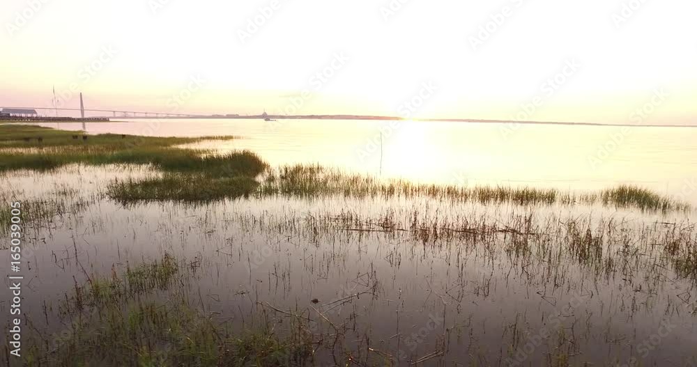 Flying over marsh grass in Charleston harbor at sunrise with a leisure boat cruising in the water. Flying over marsh grass in Charleston harbor at sunrise with a leisure boat cruising in the water.