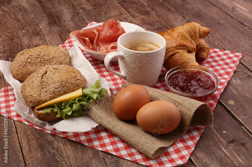 breakfast on table with bread rolls, croissants, coffe and eggs