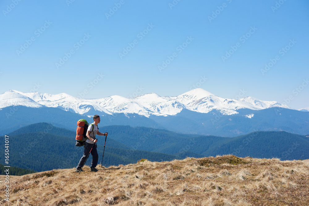 Full length shot of a man tourist with a backpack admiring the view walking on top of the mountain using hiking sticks copyspace achieving equipment athletic sportive lifestyle active