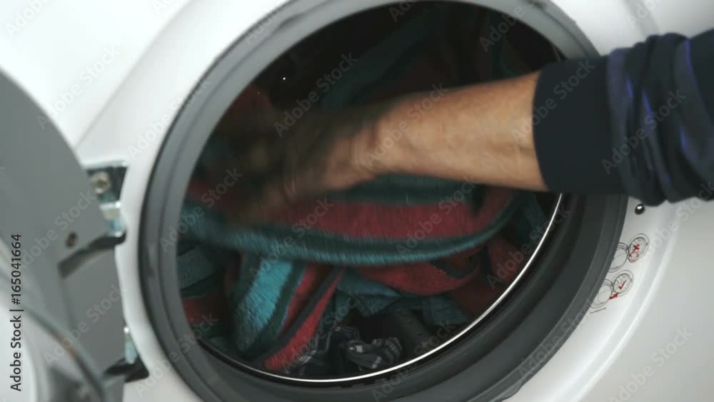 Person's hand puts a towel inside the steel drum of the washing machine