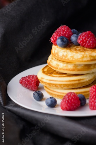 Stack of gluten free pancakes with raspberries and blueberries on white plate and black background