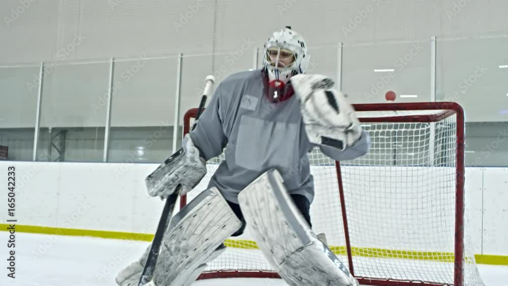 Tilt up of hockey goalie in full gear standing before net and trying to