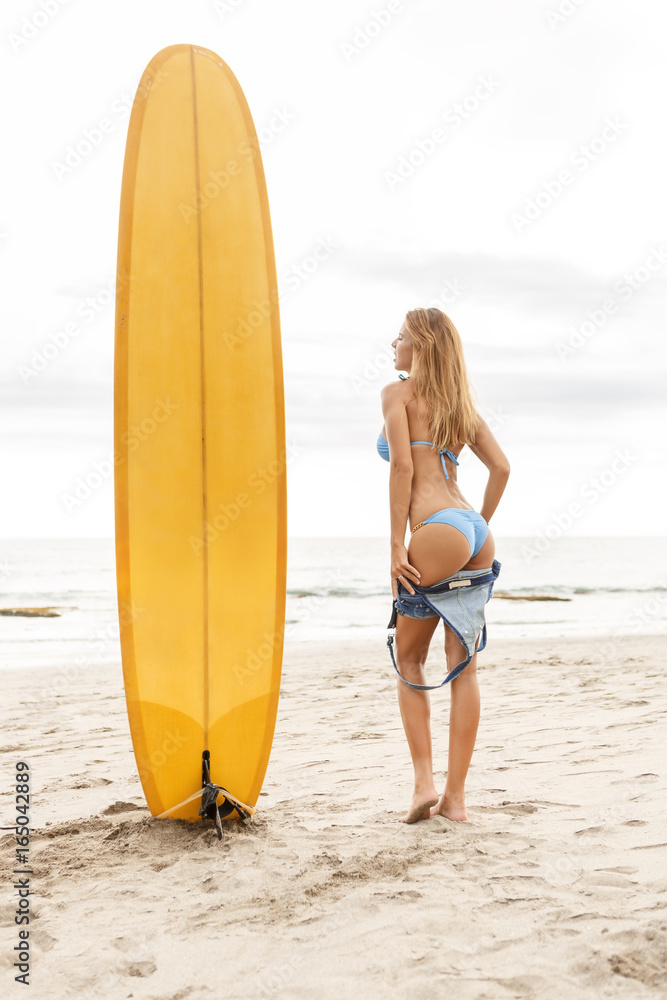 Beautiful surfing girl in sexy bikini with yellow surf longboard