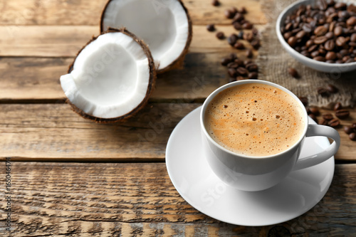 Cup of tasty coconut coffee and beans on wooden table