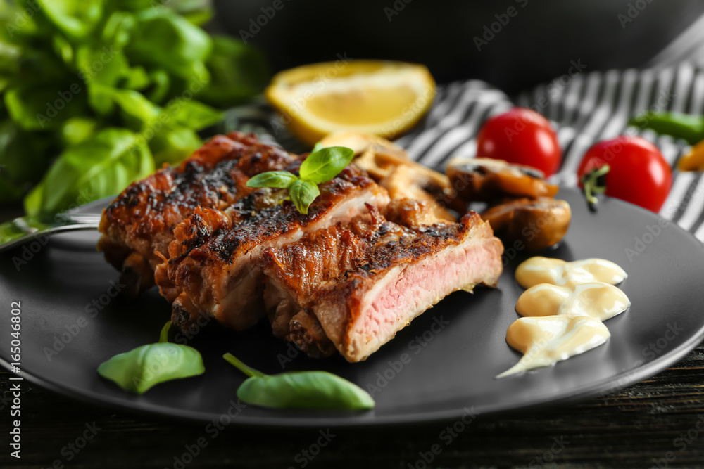 Black plate with delicious grilled sliced spare ribs with garnish on wooden table