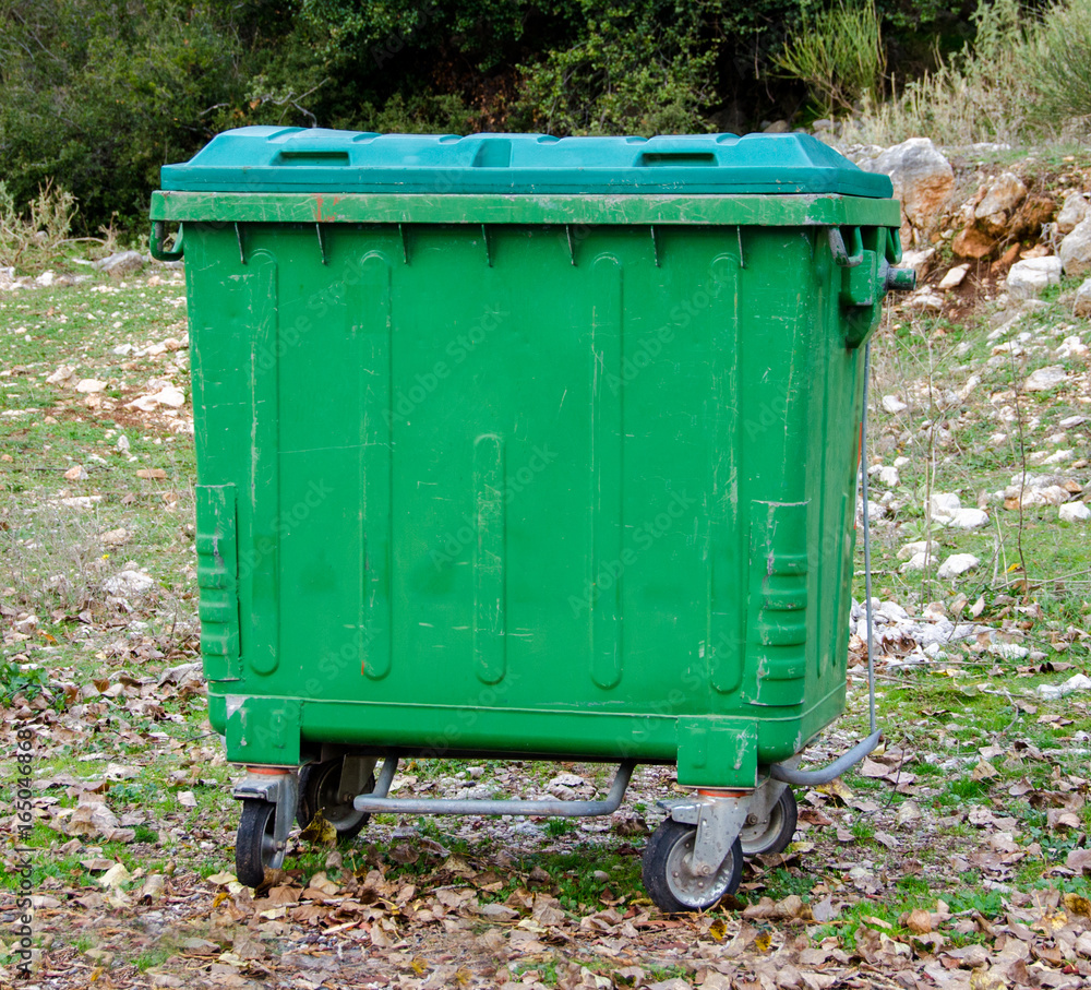 Metal green garbage can with wheels in countryside Metal green garbage can with wheels in countryside