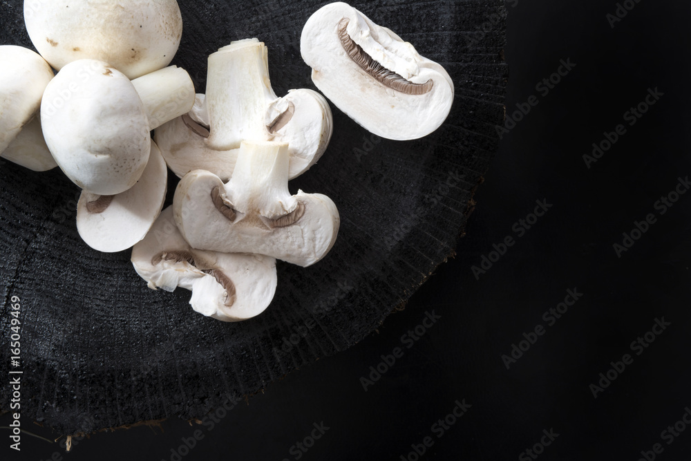 Fototapeta premium White mushrooms champignons whole and sliced on black wooden background
