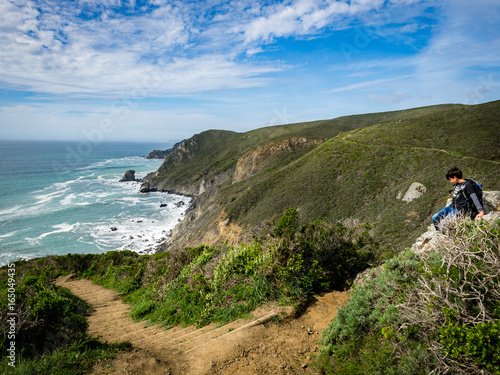 10 year old boy climbing on rocks beside trail, Pirates Cove Trail, Marin Headlands, Golden Gate National Recreation Area, California, United States
