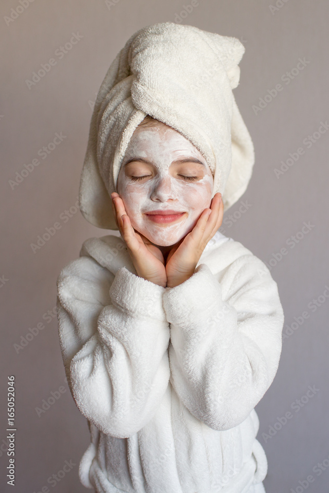 Funny little girl with a mask for skin face and with a towel on her head, portrait on a gray background