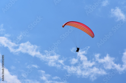 Red tandem paraglider in blue sky with fluffy white clouds