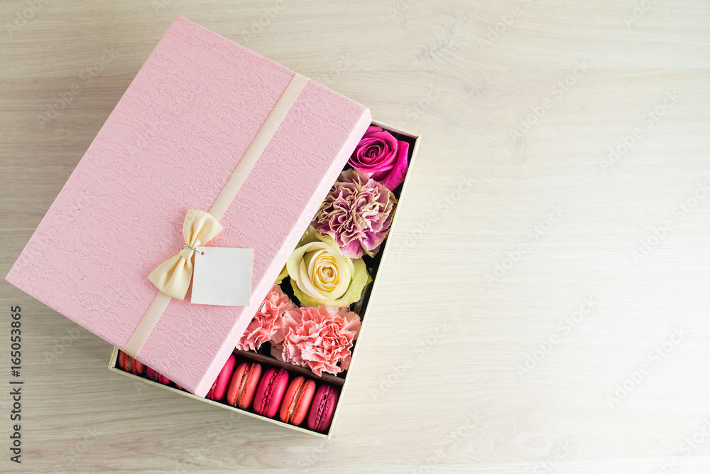 pink gift box with pink and beige roses, chrysanthemums and French sweet macaroons on light wooden background. For the celebration of different holidays