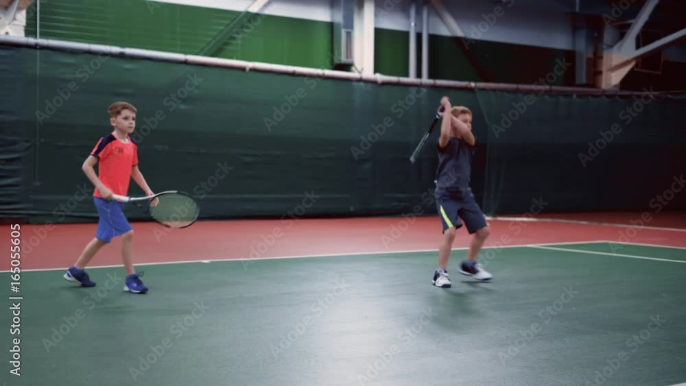 Two young boys with rackets playing tennis on court together Two young boys with rackets playing tennis on court together
