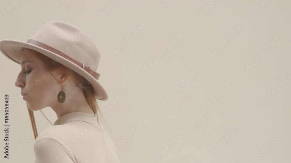 Young woman smiles and looks at the camera, posing and showing dress. Stylish girl in a hat and a lavish dress poses and smiles: backstage of a photo shoot. Young model posing on turquoise background Young woman smiles and looks at the camera, posing and showing dress. Stylish girl in a hat and a lavish dress poses and smiles: backstage of a photo shoot. Young model posing on turquoise background