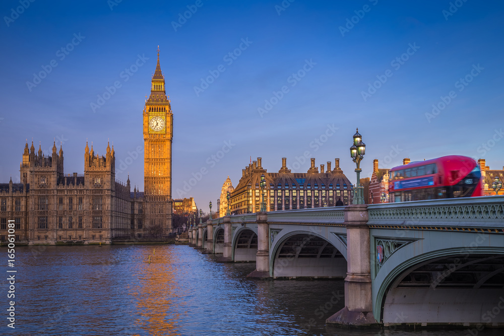 London, England - The iconic Big Ben with Houses of Parliament and traditional red double decker bus on Westminster Bridge at sunrise with clear blue sky