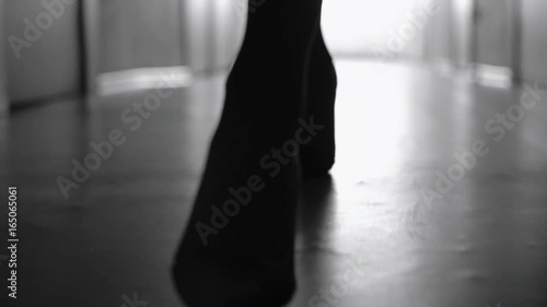 Dolly with low-section of silhouette of female legs in high heels shoes walking along corridor; black and white slow motion shot