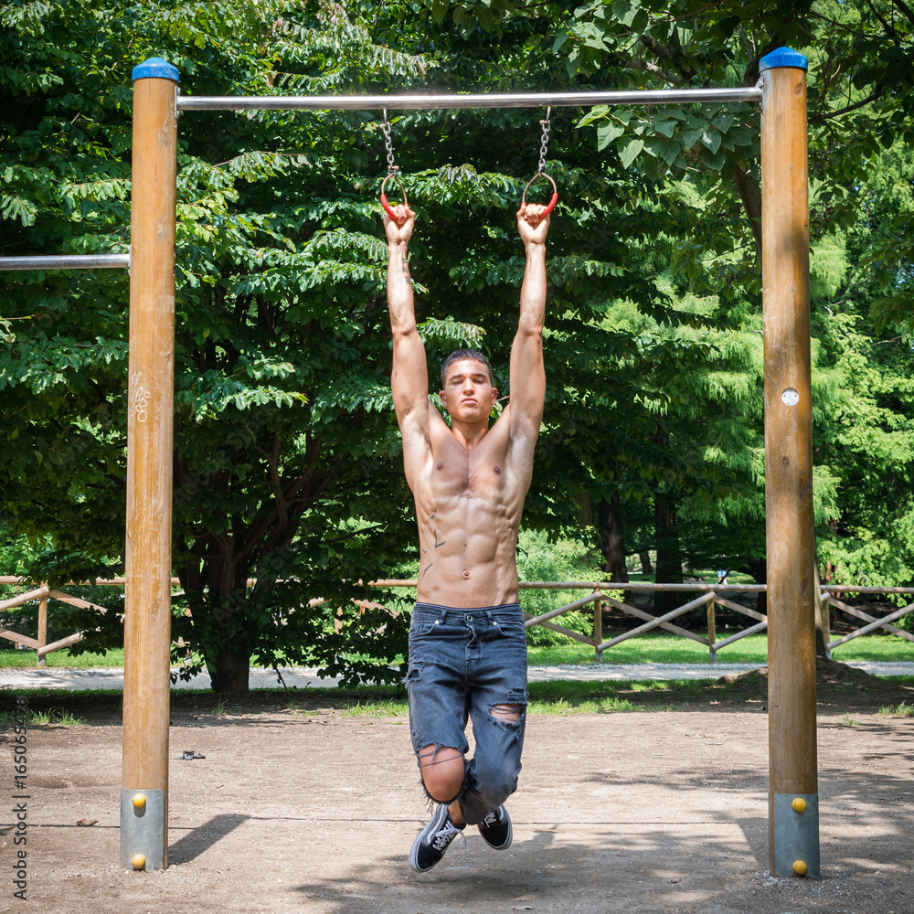 Young athletic shirtless man (20-25) exercising on monkey bars in a park Young athletic shirtless man (20-25) exercising on monkey bars in a park