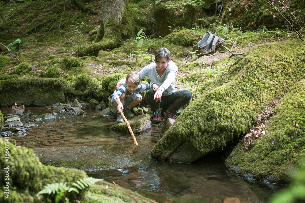 Mother and little son crouching at edge of a brook Mother and little son crouching at edge of a brook