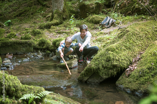 Mother and little son crouching at edge of a brook photo