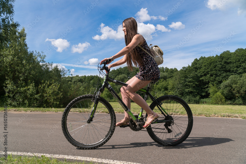 Girl riding a bicycle. Side view. Forest and clouds in the background